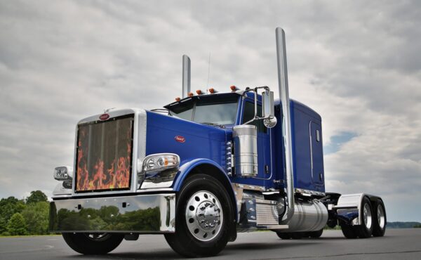 A blue semi-truck with chrome detailing and Bug Screen: Flames on the side panels, parked under a cloudy sky.