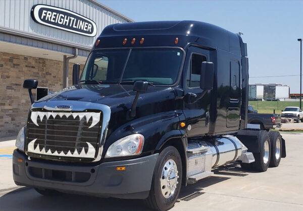 A black freightliner Jaws semi-truck parked in front of a dealership.