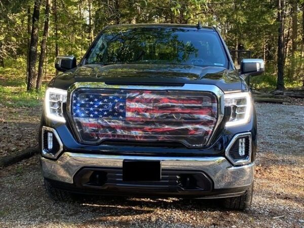 A pickup truck with an American flag grille insert parked in a wooded area.