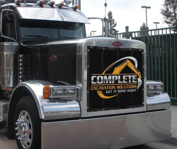 A close-up of a black Peterbilt truck with a Semi Custom Bug Screen displaying the logo "complete excavation solutions - get it done right.