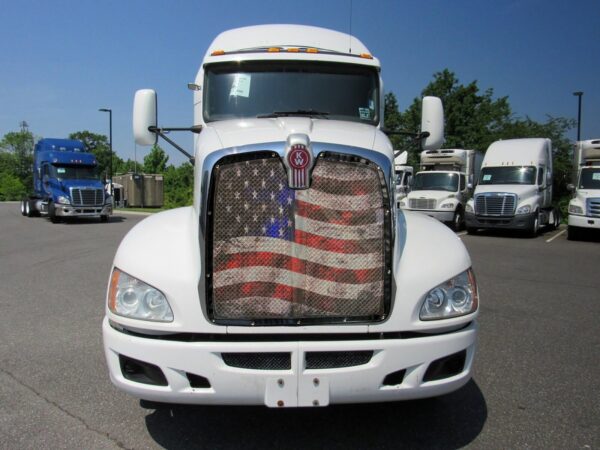 White semi-truck with an Old Glory - Bug Screen grille parked in a lot with other trucks.