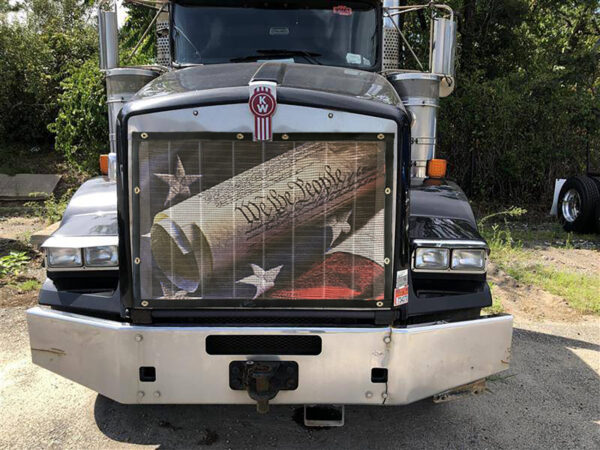 White semi-truck with a We The People - Bug Screen and a sunshade featuring the american flag design.