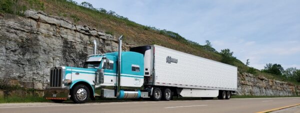 Semi-truck driving on a highway alongside a rock-cut with a Fuel Tank End Cover.