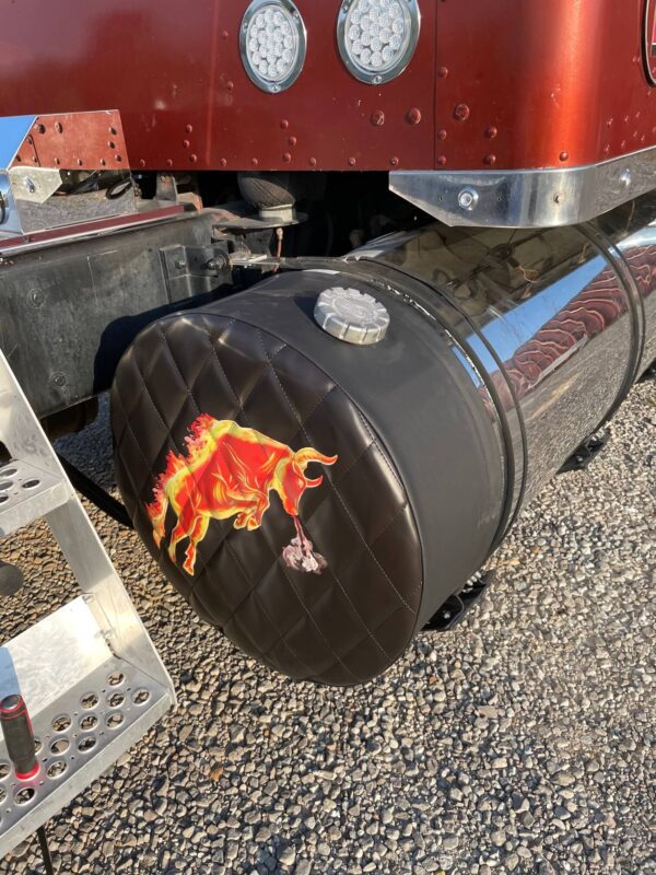 A truck's fuel tank end cover adorned with a flame design parked on gravel.