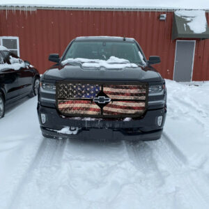 A pickup truck with an Old Glory Winter Front: 2-Zip Quilted grille cover parked on a snow-covered lot.