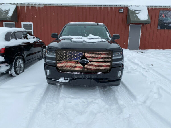 A pickup truck with an Old Glory Winter Front: 2-Zip Quilted grille cover parked on a snow-covered lot.