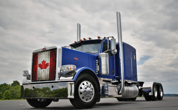 A blue semi-truck with a Canadian Flag - Semi Truck Mesh Bug Screen on the front grille, parked under a cloudy sky.