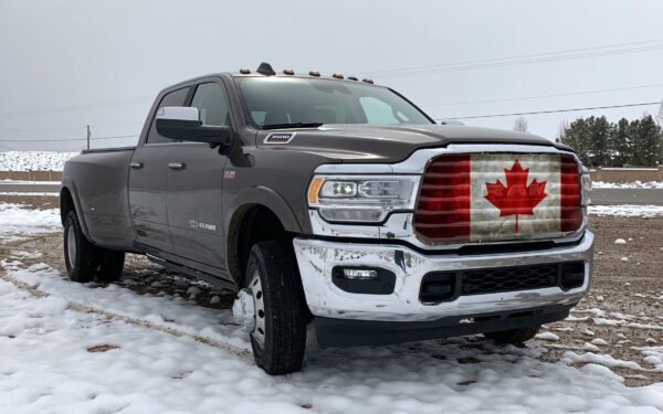 A silver ram 2500 pickup truck with a Canadian Flag- Pickup/Suv/Van Mesh Bug Screen on the grille, parked on a snowy surface.